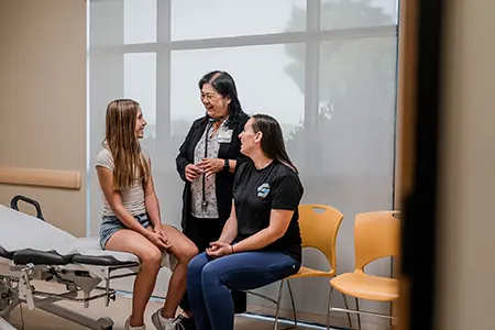 A healthcare provider talks to a young patient sitting on a bed