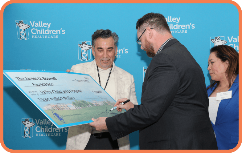 Foundation president Robert Saroyan holds a ceremonial check as it is signed by a representative of the Boswell Company